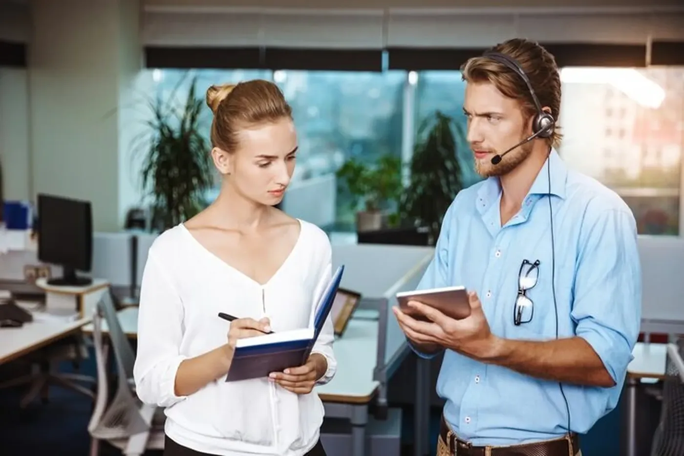 Two customer support colleagues, one wearing a headset, reviewing a tablet