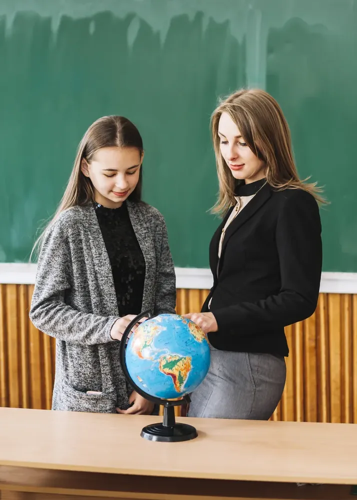 A teacher and a student looking at a globe together in a classroom