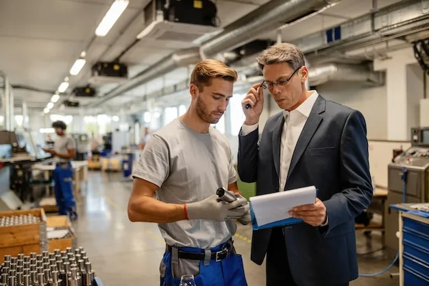 An engineer reviewing a tablet with a machine operator on the factory floor