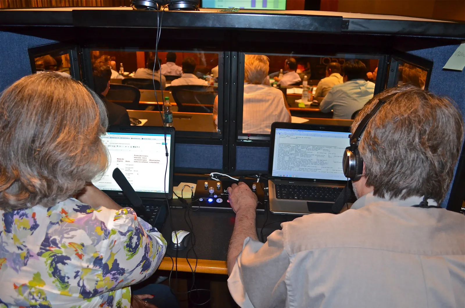Two simultaneous interpreters share a booth overlooking a meeting room